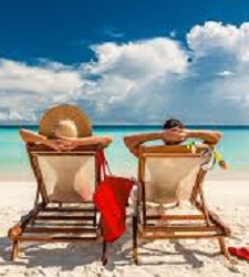 Two people lying on two lounge chairs facing the beach